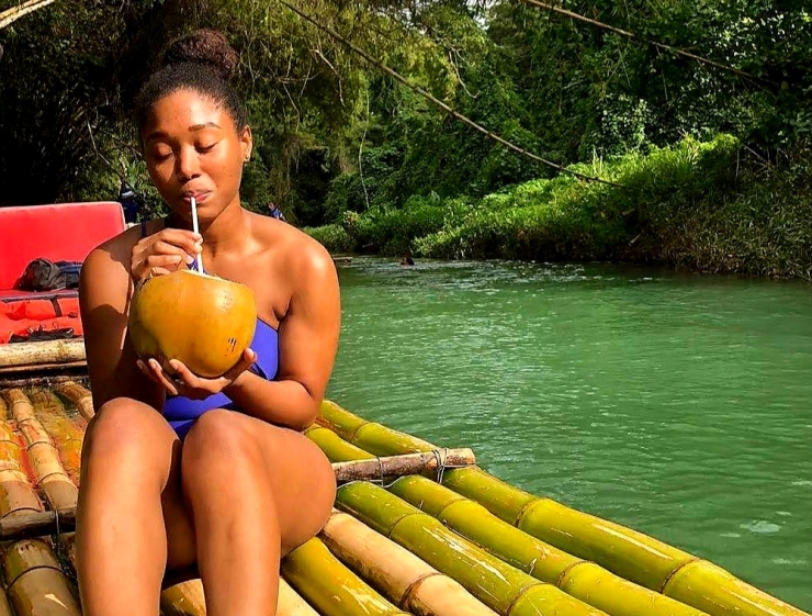 Girl sipping from coconut on a bamboo raft at Martha Brae